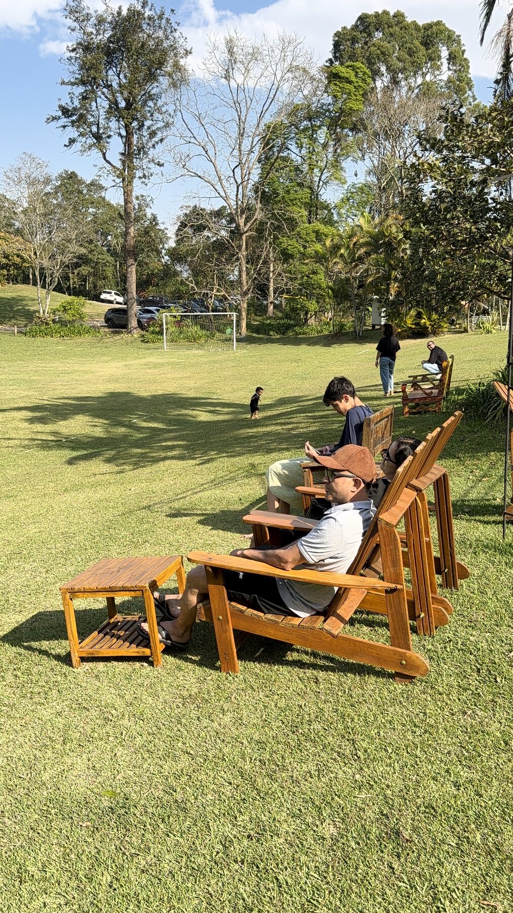 Famílias descansando em cadeiras de madeira diante do gramado